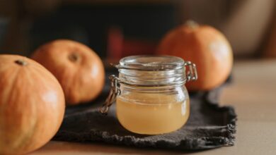 A cozy still life with homemade apple cider in a glass jar surrounded by pumpkins on a wooden table.