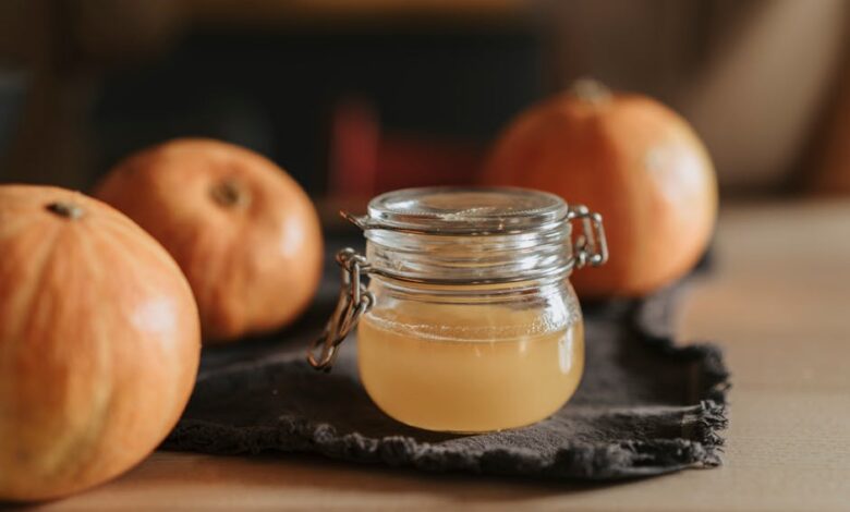 A cozy still life with homemade apple cider in a glass jar surrounded by pumpkins on a wooden table.